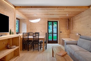 A wooden interior with a dining area, sofa, TV, and a door leading outside.