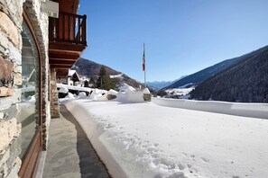 A snow-covered balcony with a stone wall, a flag, and a mountainous landscape in the background.