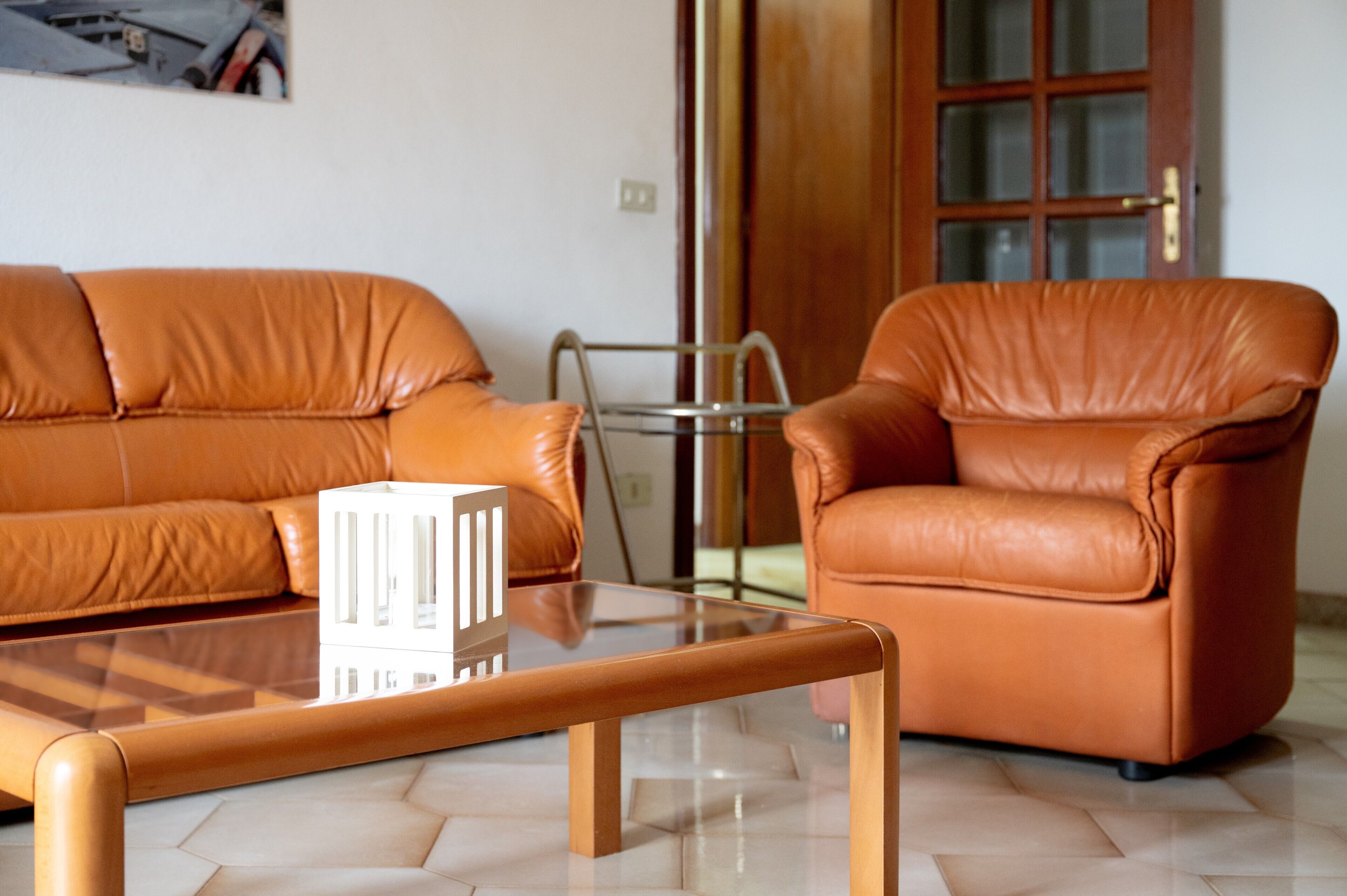 A room with a glass coffee table, a brown leather sofa, and a brown leather armchair.