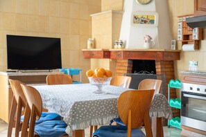 A dining area with a table set for four, a television, a fireplace, and kitchen cabinets.