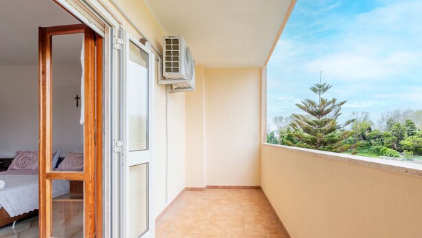 A balcony with a view of greenery, a sliding glass door leading to a bedroom, and an air conditioning unit mounted on the wall. - Apartment 'Baldi' with Private Terrace, Wi-Fi and Air Conditioning (Otranto)