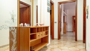 A hallway with a wooden console table, a tiled floor, and a mirror reflecting a door and a staircase. - Apartment 'Baldi' with Private Terrace, Wi-Fi and Air Conditioning (Otranto)