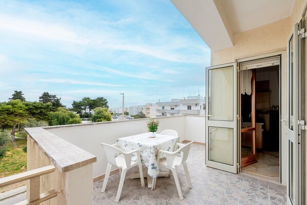 A balcony with a table and chairs, a view of the city, and a sliding door leading to a kitchen.