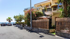 A coastal hotel with a fenced entrance, a balcony with potted plants, and a view of the sea. - Apartment 'Holiday Home Castello' with Sea View, Wi-Fi and Air Conditioning (Aci Castello)