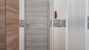 A bathroom with a wooden door, tiled walls, and a shower area. - Apartment 'Holiday Home Castello' with Sea View, Wi-Fi and Air Conditioning (Aci Castello)