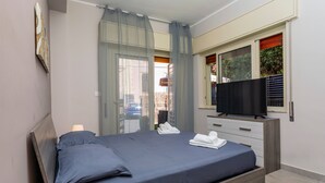 A bedroom with a bed, a TV, a window with blinds, and a door. - Apartment 'Holiday Home Castello' with Sea View, Wi-Fi and Air Conditioning (Aci Castello)