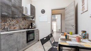 A modern kitchen with grey cabinets, a stove, and a dining area with a table and chairs. - Apartment 'Holiday Home Castello' with Sea View, Wi-Fi and Air Conditioning (Aci Castello)