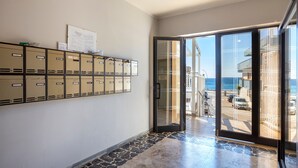 A hallway with storage lockers, a glass door leading to a balcony with a view of the sea, and a tiled floor.
