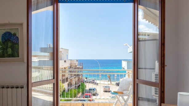A room with a large window overlooking a street and the sea.
