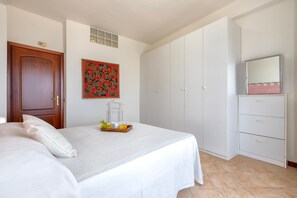 Een slaapkamer met een bed, een dressoir, een spiegel en een decoratief wandobject.