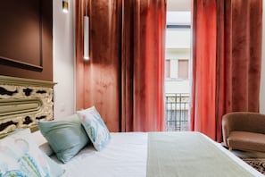 A hotel room with a bed, pillows, a chair, curtains, a balcony, and a decorative headboard.