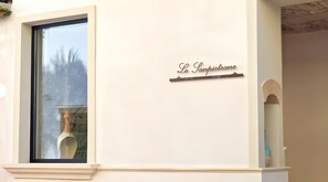 Una ventana con un letrero de metal que dice 'Le Sanpietrane' en la pared.