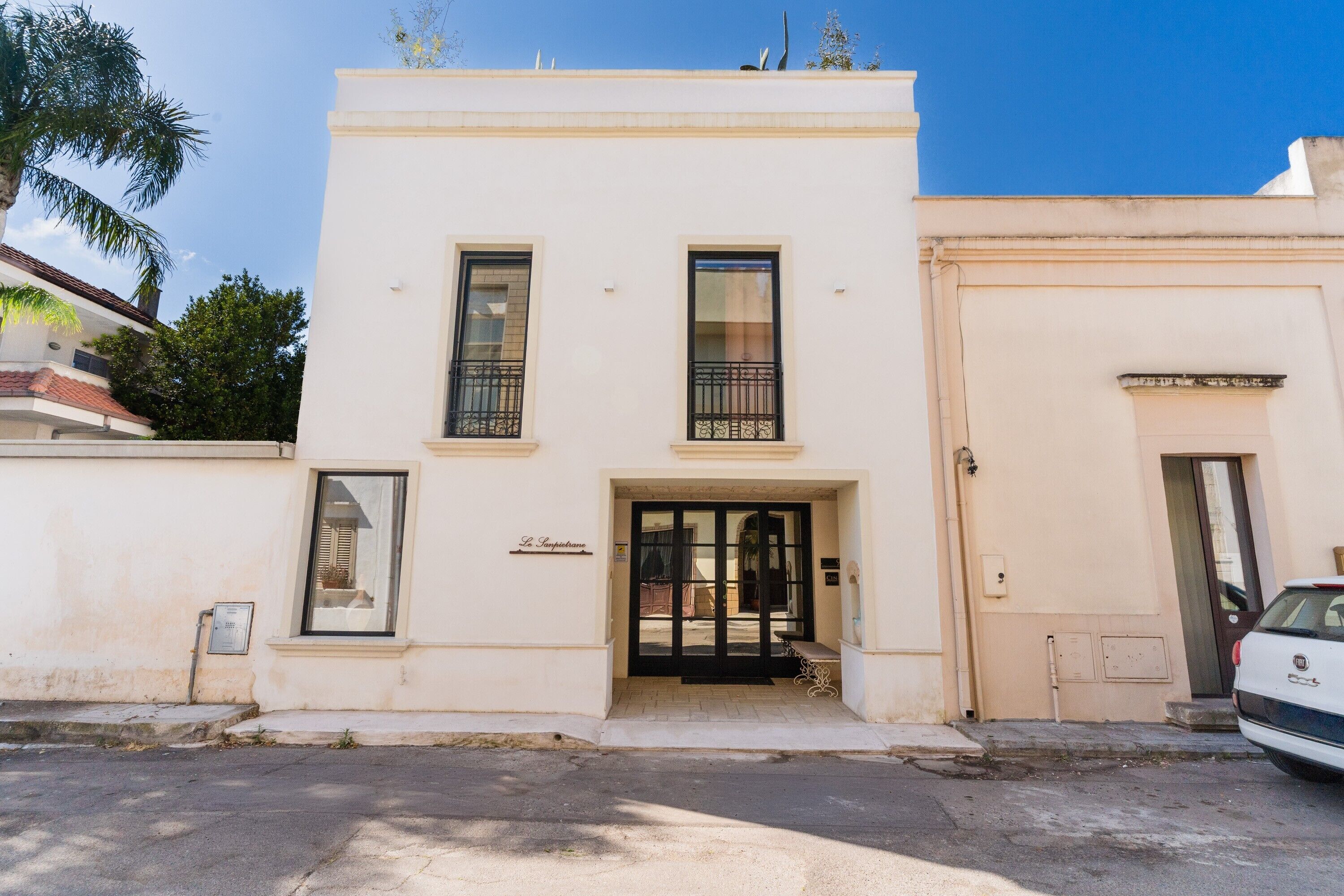 Un edificio a due piani con facciata bianca, una porta d'ingresso nera e un piccolo balcone con ringhiere in metallo.