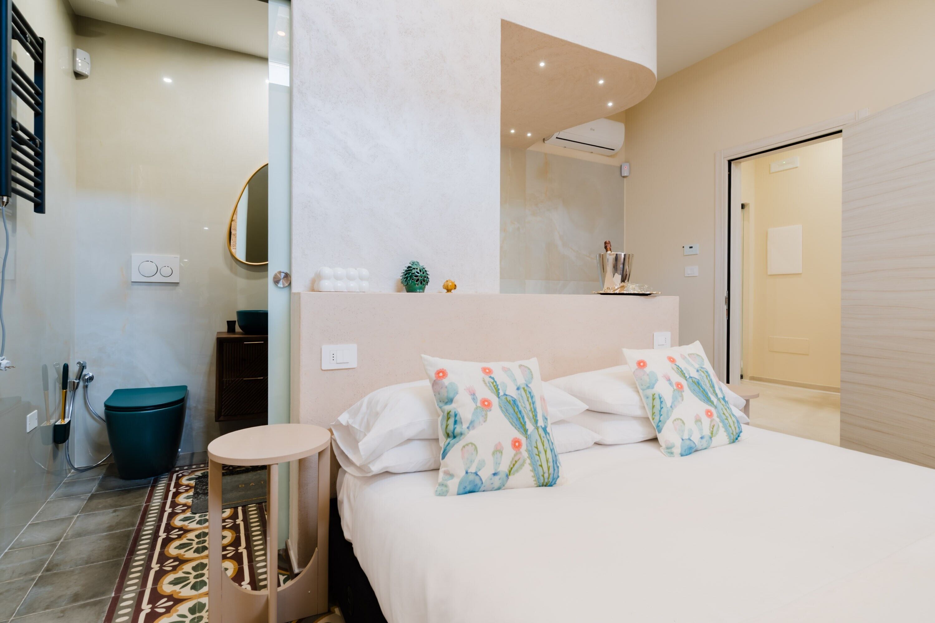 A modern bedroom with a bed, bedside tables, a small round table, a mirror, and a shower area.