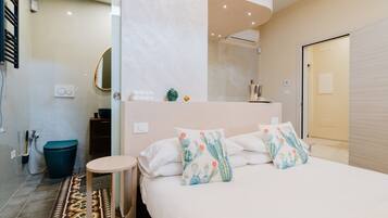 A modern bedroom with a bed, bedside tables, a small round table, a mirror, and a shower area.