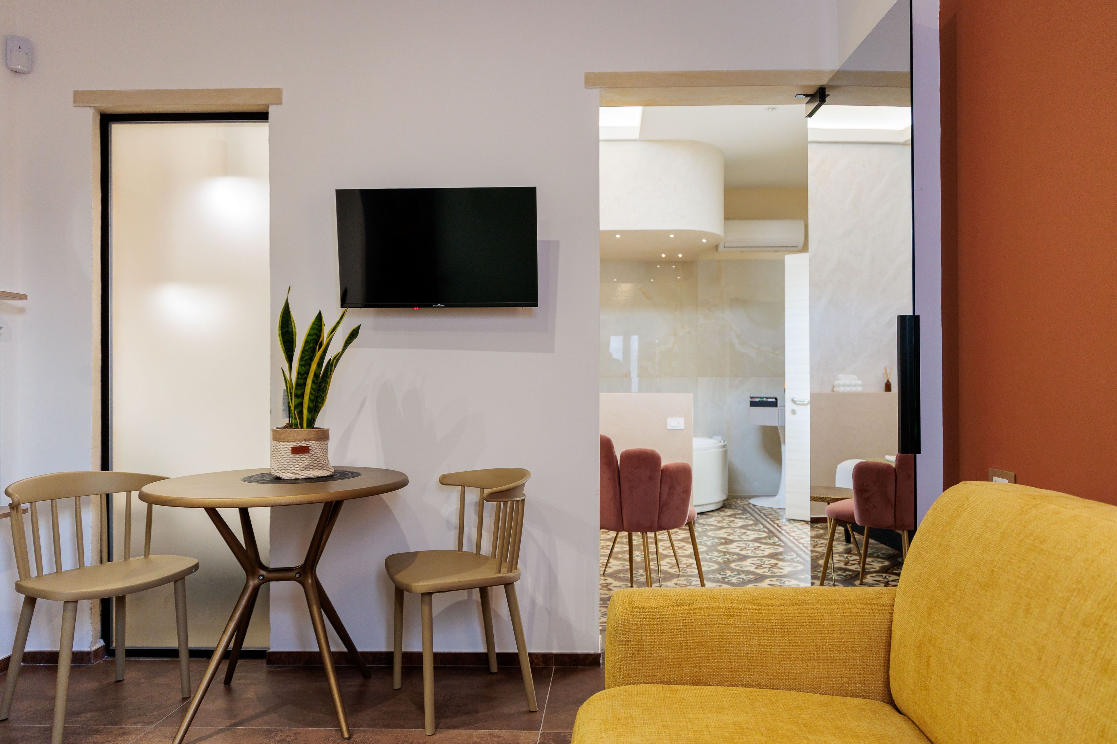 Ein modernes Wohnzimmer mit einem runden Tisch, vier Stühlen, einem Flachbildfernseher und einem gelben Sofa.