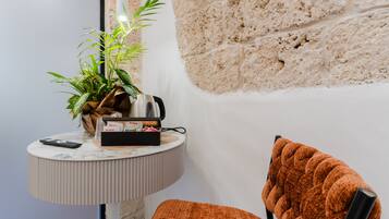 Un coin de pièce avec une table ronde, une plante en pot, une télécommande et une chaise dotée d’un coussin texturé.