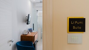 A hotel room with a blue chair, a small wooden table, a television mounted on the wall, a sign indicating the room is the 'Li Pumi Suite,' and a keypad lock. - Room 'Li Pumi' with Shared Terrace, Wi-Fi and Air Conditioning (Taviano)