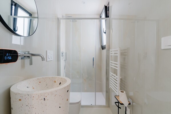 Ein Badezimmer mit freistehender Waschbecken, einer Duschkabine aus Glas und einer digitalen Uhr.