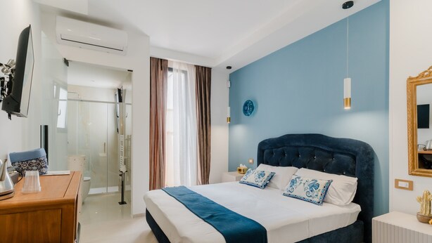 A modern hotel room with a large bed, a desk, a mirror, and a wall-mounted TV. - Room 'Li Pumi' with Shared Terrace, Wi-Fi and Air Conditioning (Taviano)
