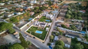 An aerial view of a residential area with a large, rectangular building featuring a swimming pool, solar panels, and a well-maintained lawn.