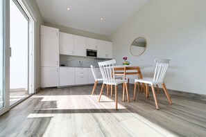 A modern kitchen with white cabinets, a marble countertop, and a dining area with a round table and white chairs.