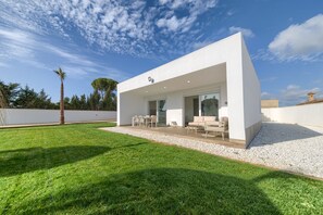 A modern house with a covered patio, a lawn, and a clear sky.