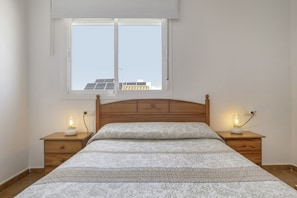 Une chambre à coucher avec une tête de lit en bois, une grande fenêtre donnant sur des panneaux solaires, deux tables de chevet avec des lampes et une couvre-lit à motifs.