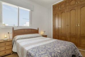 A bedroom with a bed, wooden wardrobe, and a window with a view of buildings. - Apartment 'Antonia Conil' with Shared Terrace, Wi-Fi and Air Conditioning (Conil de la Fra.)