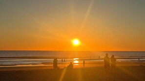 A beach scene with the sun setting over the ocean, silhouettes of people on the sand, and a clear sky. - Apartment 'Antonia Conil' with Shared Terrace, Wi-Fi and Air Conditioning (Conil de la Fra.)
