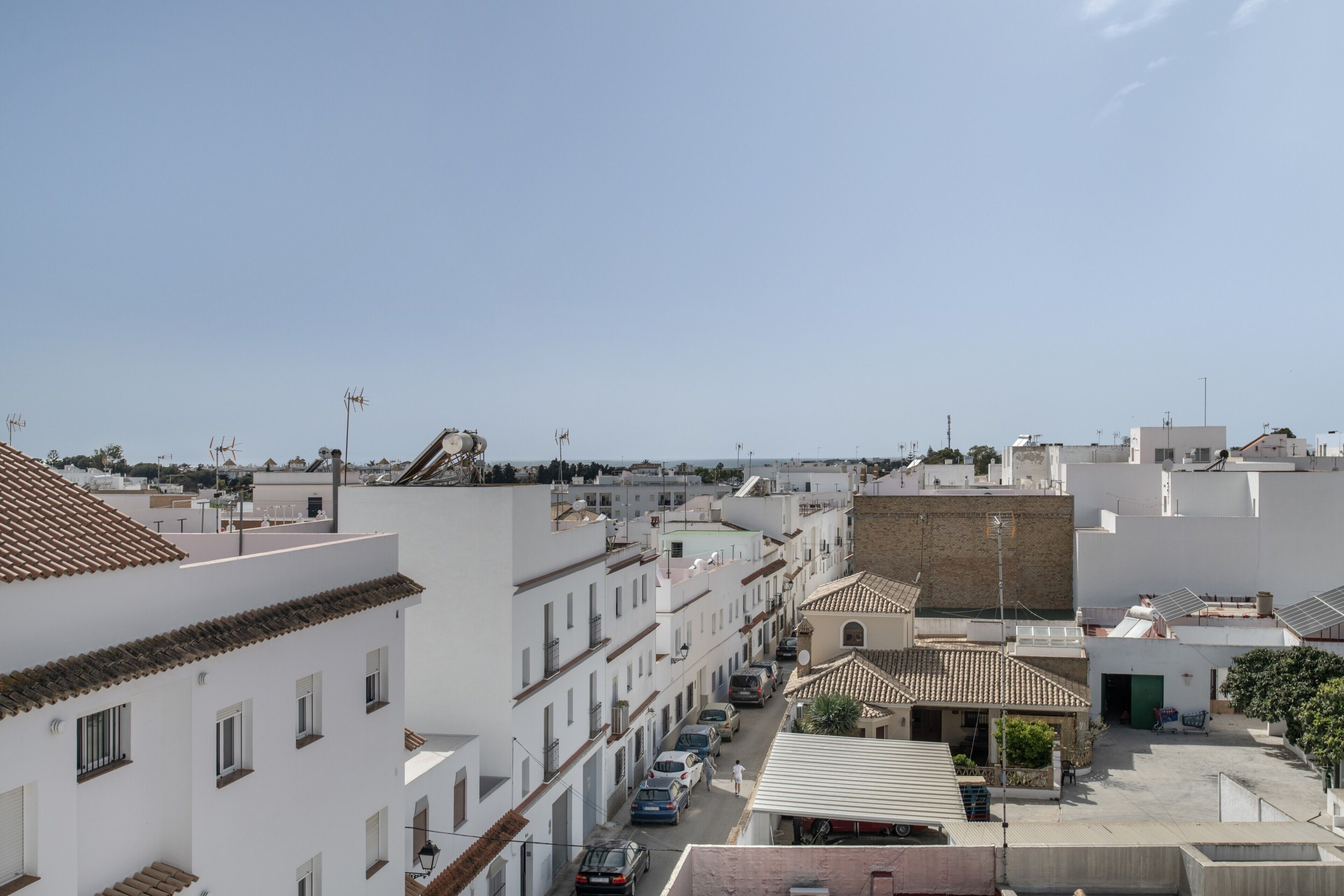 Une rue résidentielle bordée d’immeubles blancs, avec un ciel dégagé et des voitures garées.