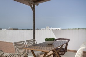 A wooden table with a bowl of plants, wicker chairs, and a view of a cityscape.