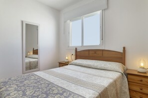 A bedroom with a bed, a nightstand, a bedside lamp, a window, and a mirror.