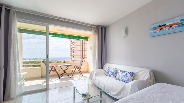 A hotel room with a balcony, a sofa, a bed, and a painting on the wall.