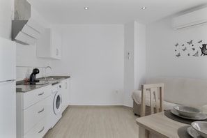 Una cocina moderna con lavadora, una mesa de comedor con platos y un sofá.