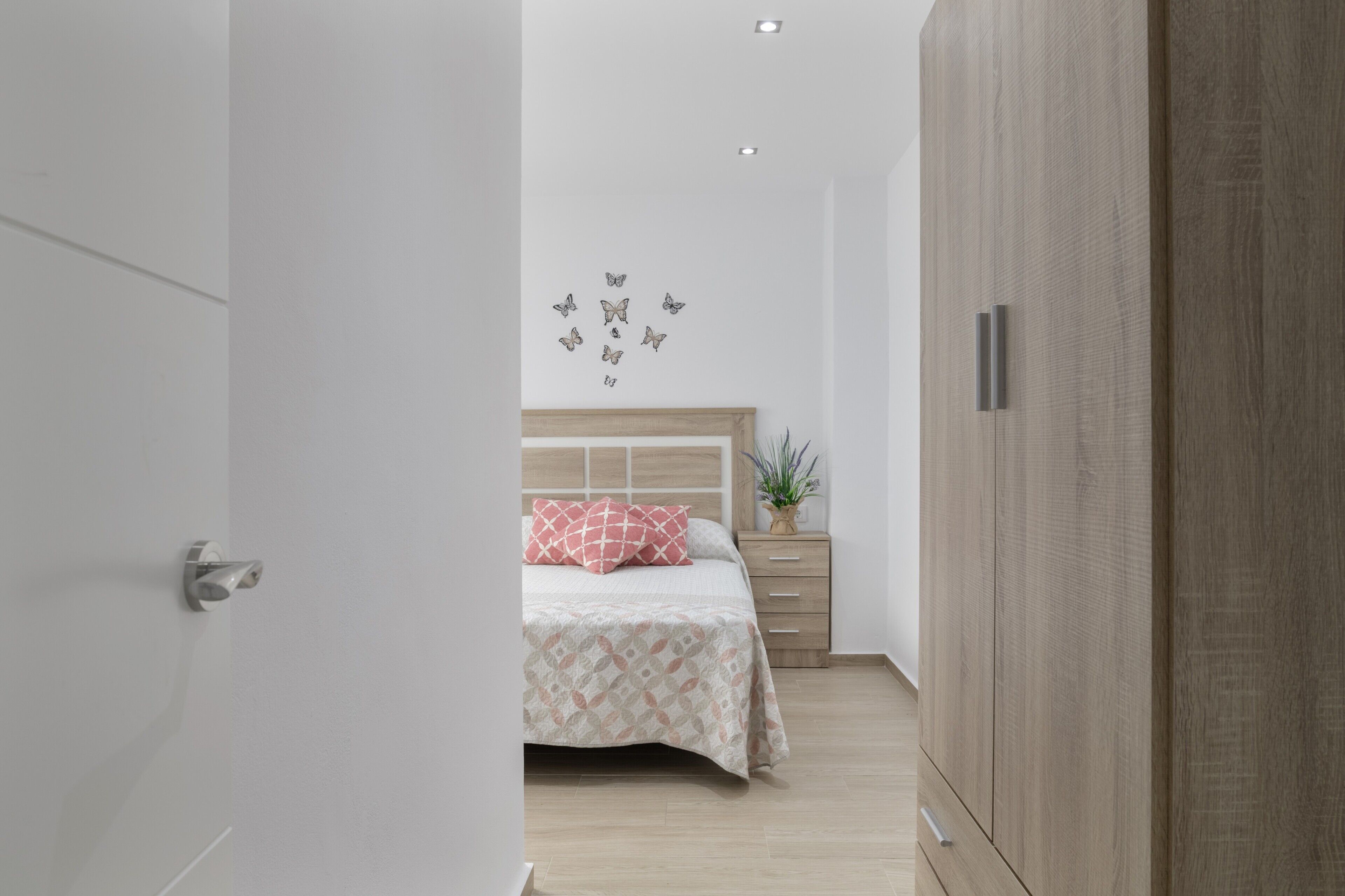 A bedroom with a bed, a nightstand, a wardrobe, and a wall with butterfly decals.