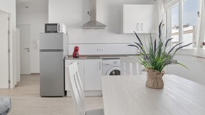 Eine moderne Küche mit weißen Schränken, einer Mikrowelle, einem roten Wasserkocher, einer Waschmaschine und einem großen Fenster mit Vorhängen.
