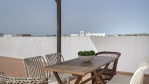 Eine Terrasse im Freien mit Holztisch, Korbstühlen und einem Blumentopf.