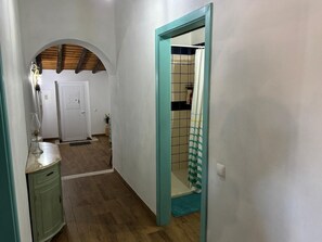 A hallway with a wooden floor, a white door, a cabinet, and a bathroom visible through an open door.