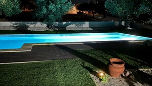 Piscina com deck revestido, cercada por grama e árvores.