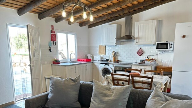 Uma sala de estar aconchegante com sofá e almofadas, uma cozinha com máquina de lavar e uma área de jantar com mesa e cadeiras.