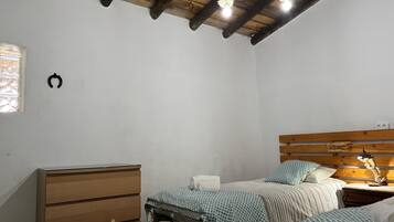 A bedroom with a wooden headboard, two beds with patterned bedding, a wooden dresser, and a hanging light fixture.