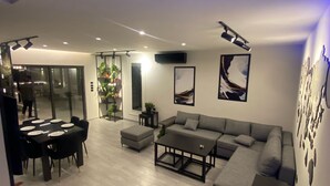 A modern living room with a sectional sofa, a coffee table, and a dining area with a table set for four. - Lava villas (Ma'In)