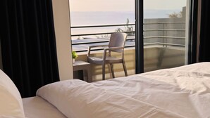 A hotel room with a large window offering a view of the sea and a balcony with a chair. - Lava villas (Ma'In)
