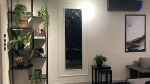 A modern dining area with a black table, white plates, and a black chair. There is a black bookshelf with plants and a black-framed window. - Lava villas (Ma'In)