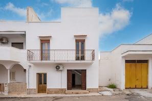 A two-story building with a balcony, a wooden door, and a yellow garage door.