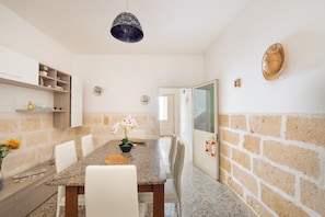 A dining area with a granite table, white chairs, a hanging light fixture, and a brick wall.