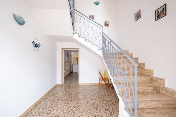 A staircase with a metal railing, a polished stone floor, and a door leading to another room.