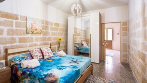 A bedroom with a brick wall, a bed with a blue ocean-themed bedspread, a hanging light fixture, and a door leading to another room. - Holiday Home 'Residenza Della Riva Blu' with Sea View, Shared Terrace and Air Conditioning (Porto Cesareo)
