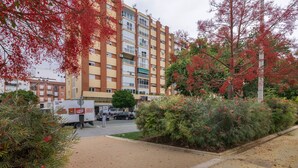 Un immeuble à plusieurs étages doté de balcons, d’une zone pavée et d’un camion garé devant.